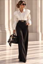 Pantalon Rive Gauche noir taille haute à jambes longues, porté avec une blouse blanche à volants